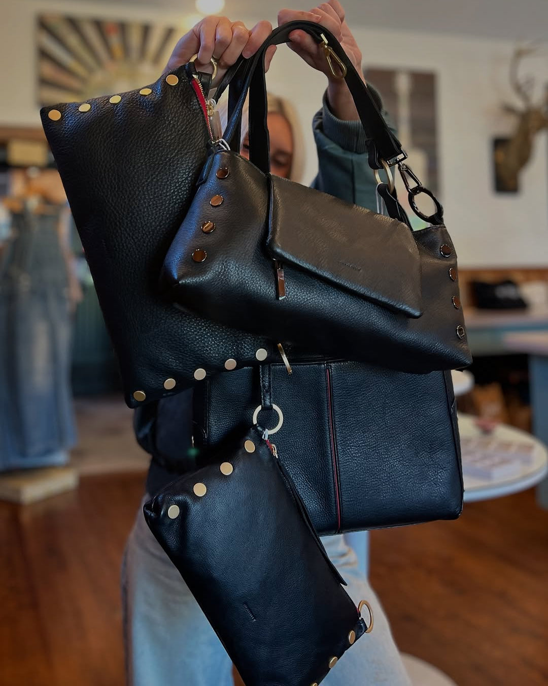 Person holding a black leather handbag with gold studs in an indoor setting