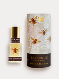 A glass bottle of Tokyo Milk Honey and the moon Parfum with a floral design and bees on the label, next to its packaging.