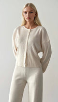 Woman wearing a beige cardigan and pants against a plain background