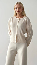 Woman wearing a beige cardigan and pants against a plain background