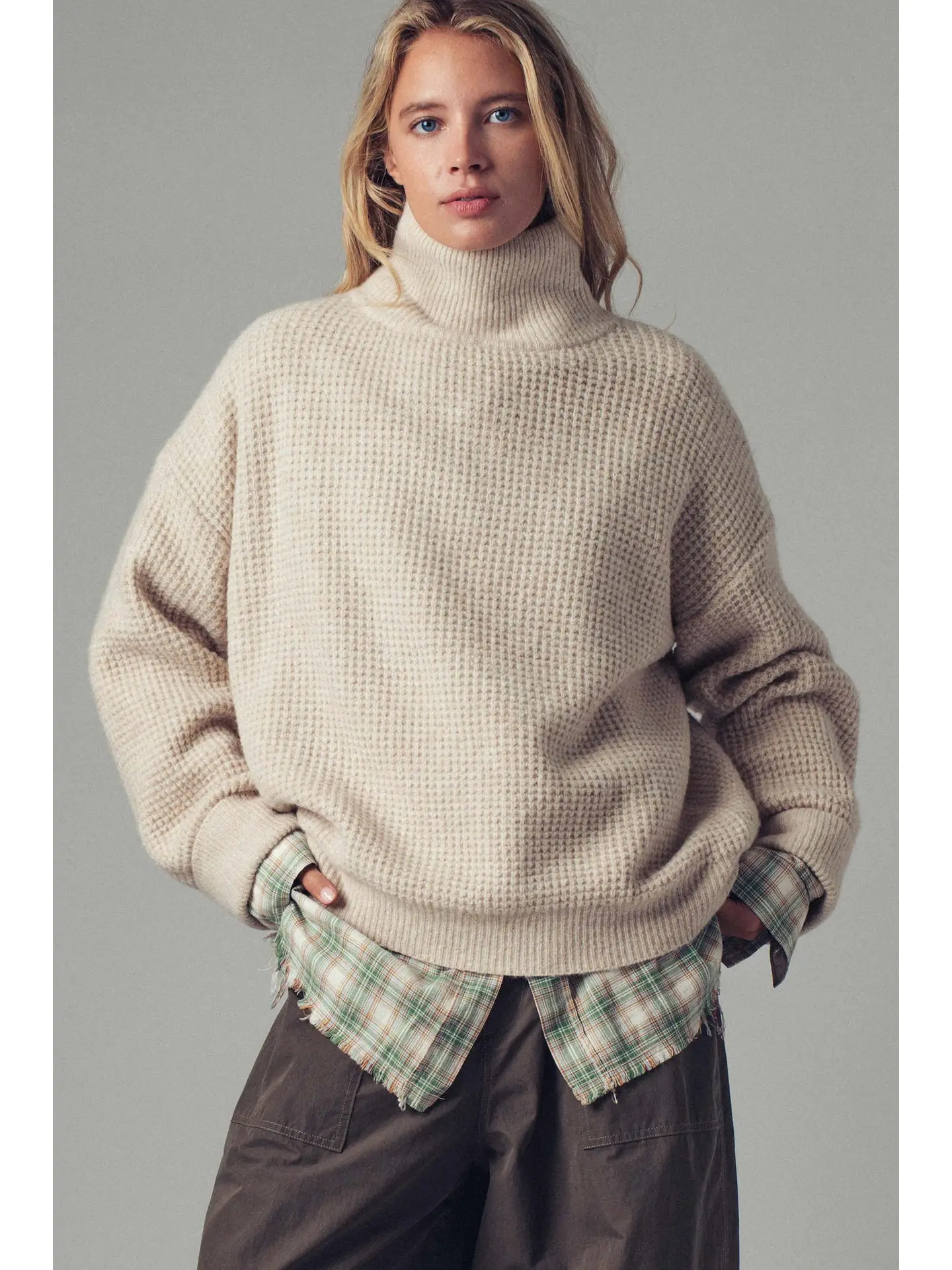 Person wearing a beige sweater over a plaid shirt with a plain background