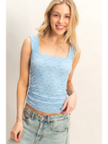 Woman wearing a light blue sleeveless top and jeans against a plain background