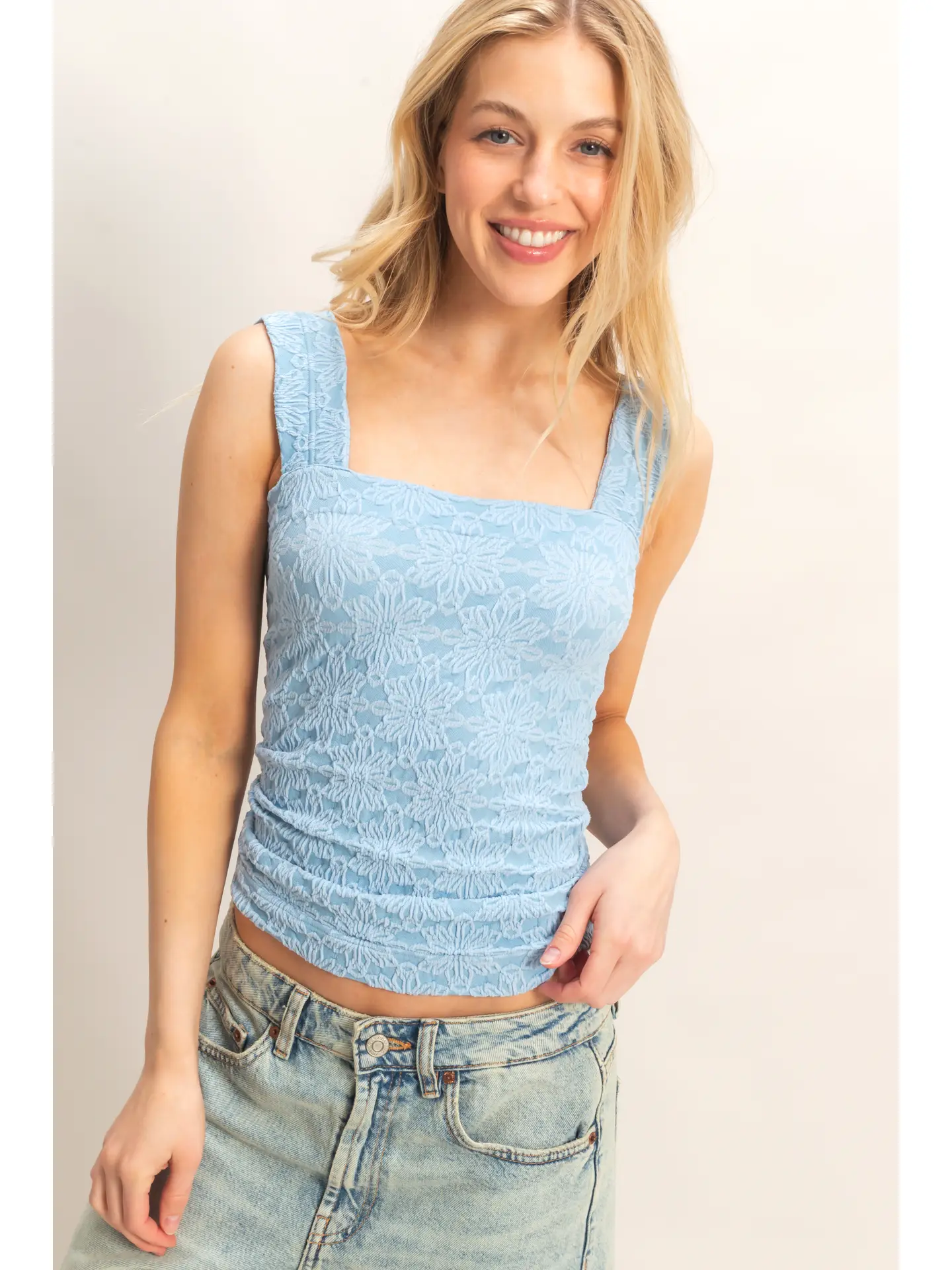 Woman wearing a light blue sleeveless top and jeans against a plain background